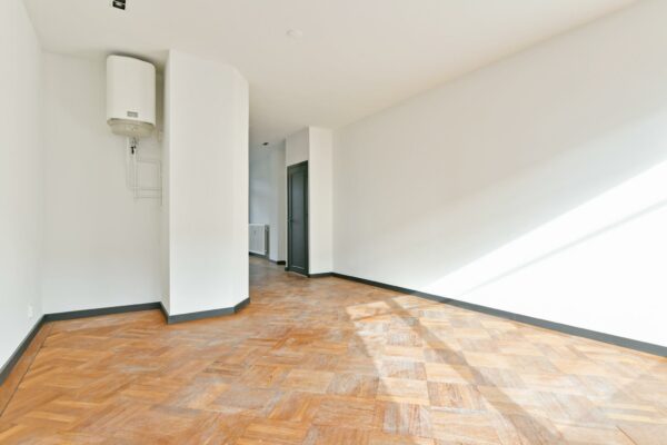 Lichte, lege kamer aan de Cornelis Dopperkade met houten visgraatvloer, witte muren en een boiler aan de muur.